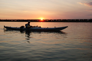 Photo of a kayaker paddling in the sunset with a train off in the distance